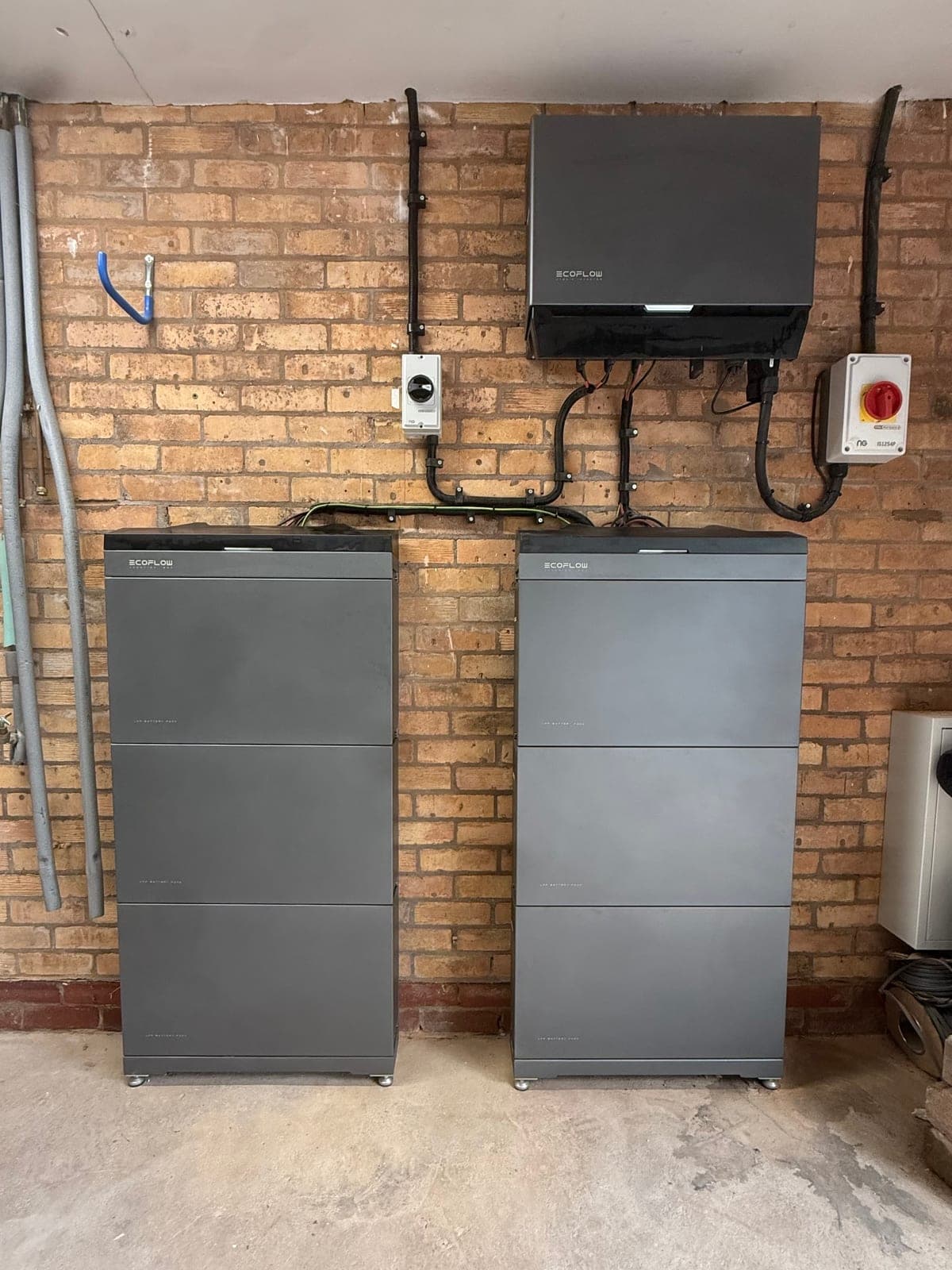 Two stacked EcoFlow home batteries with inverter, labelled and wired clean against a brick wall
