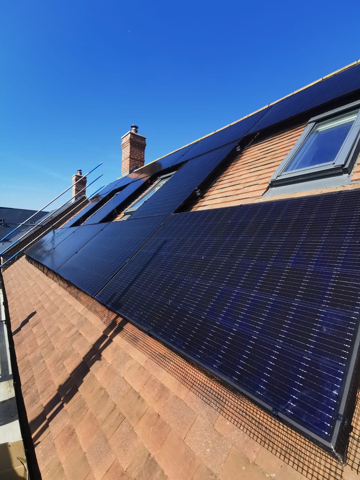 Black solar panels on a tiled red-brick roof with Velux skylights